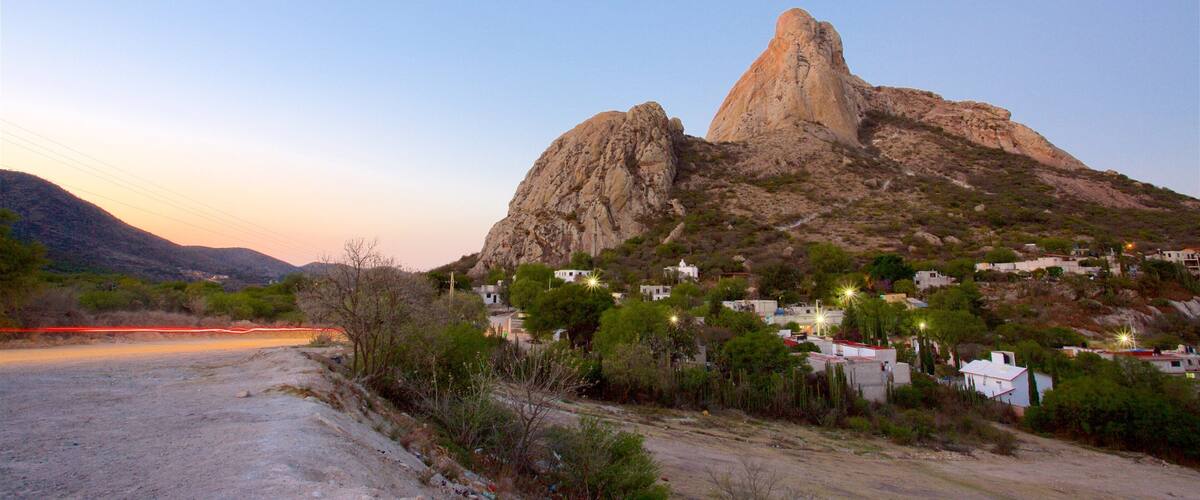 A rocky mountain with a prominent peak, a small village with houses, and a dirt road.