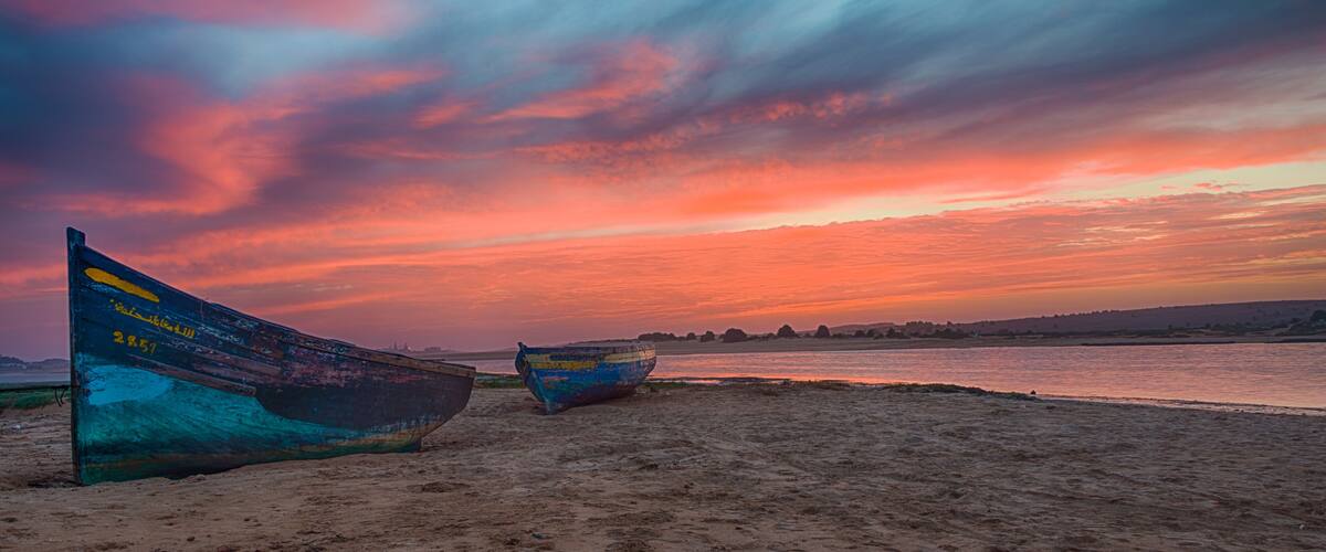 Two boats on a sandy beach with a sunset sky.