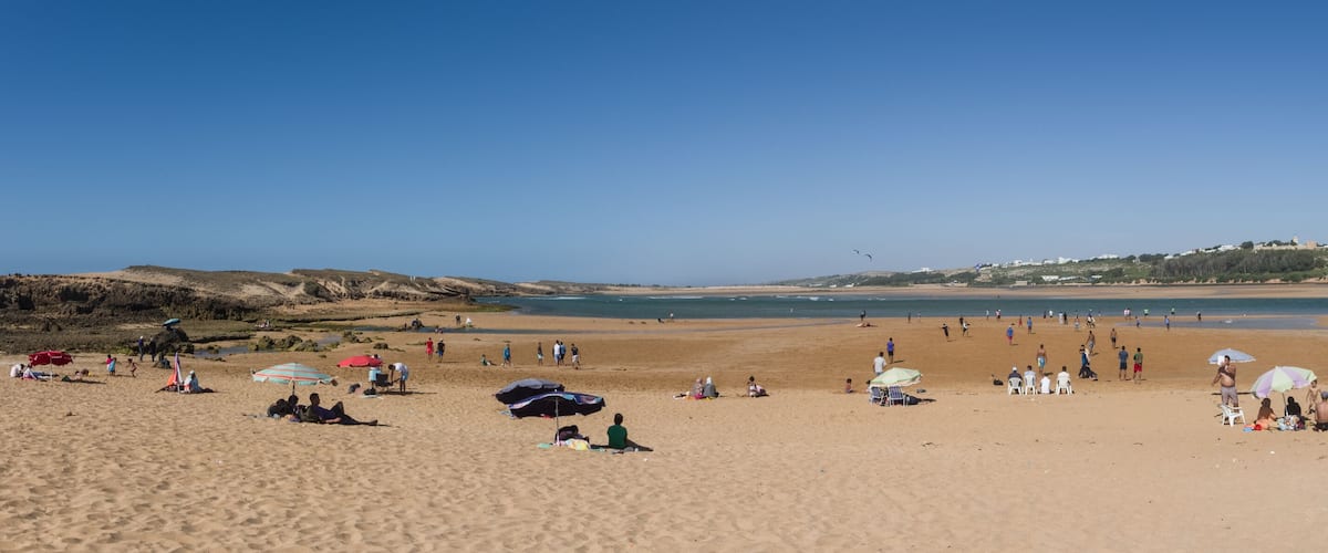 A sandy beach with people, umbrellas, and a clear blue sky.