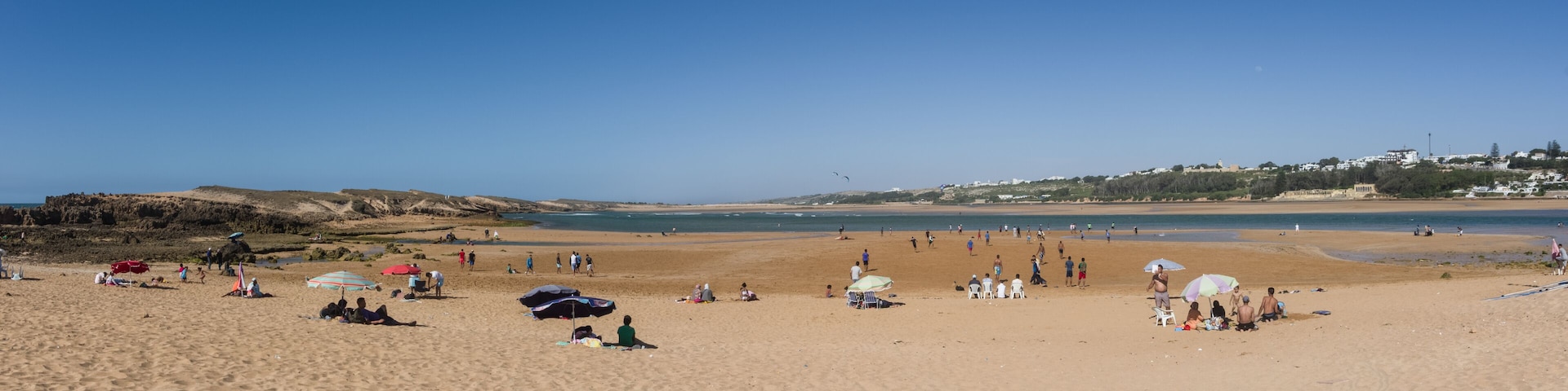 A sandy beach with people, umbrellas, and a clear blue sky.