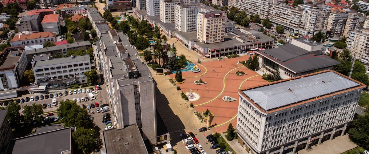 An aerial view of a city with a central square surrounded by buildings and a parking lot.