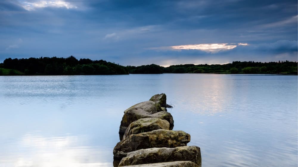 Eine Steg, der sich in ruhiges Wasser unter einem bewölkten Himmel erstreckt.