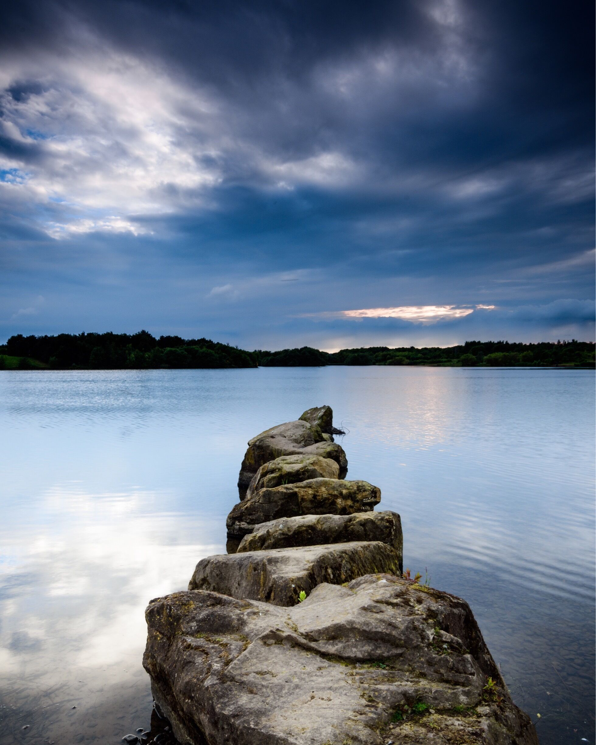 A stone pier extending into calm water under a cloudy sky.