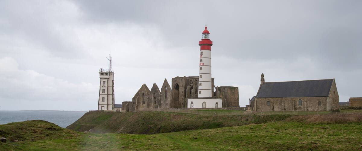 A coastal lighthouse with a red top, a white tower, and a church with a steep roof.