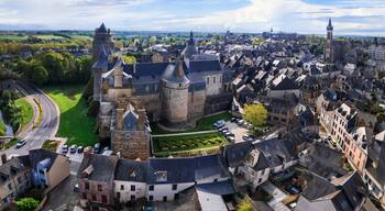 Une ville historique, avec un château imposant, des rues étroites et une végétation luxuriante aux alentours.
