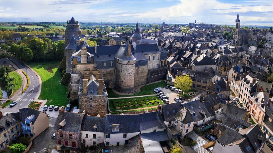 Un pueblo histórico con un castillo destacado, calles estrechas y zonas verdes circundantes.