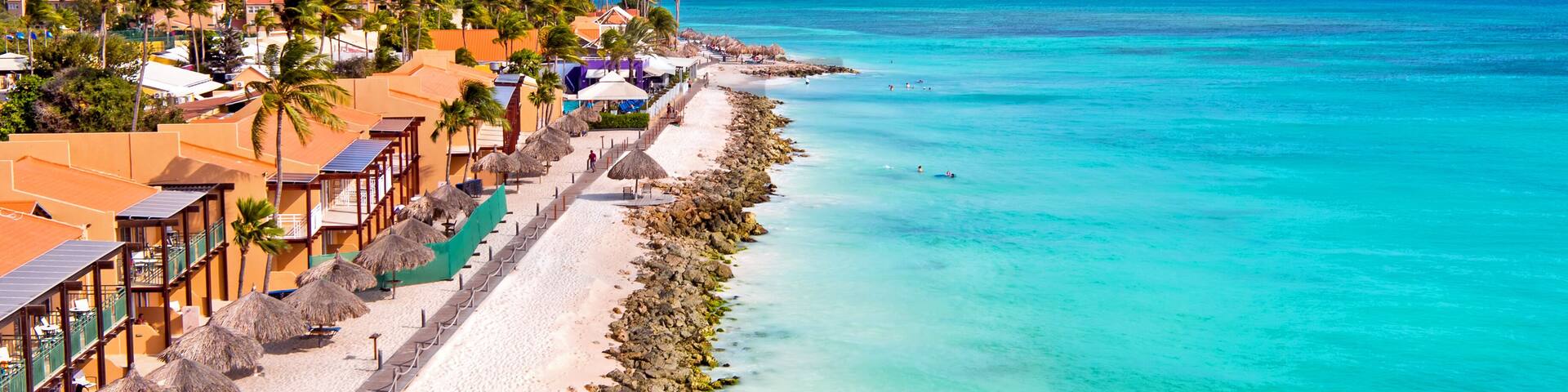 A coastal resort with a white sandy beach, turquoise waters, palm trees, and overwater bungalows.