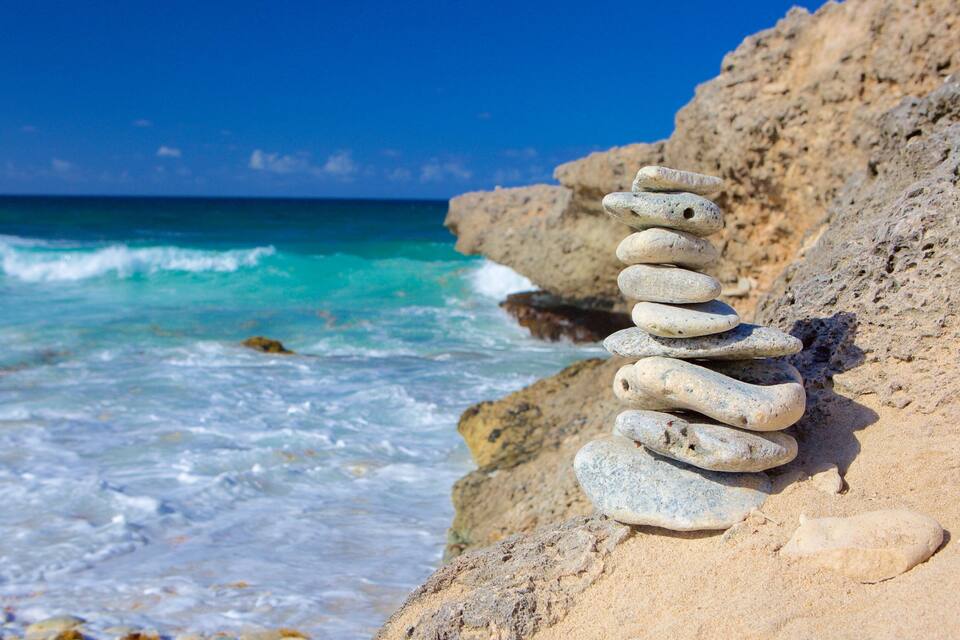 Ein Stapel glatter, abgerundeter Steine an einem felsigen Strand, im Hintergrund türkisfarbene Wellen.
