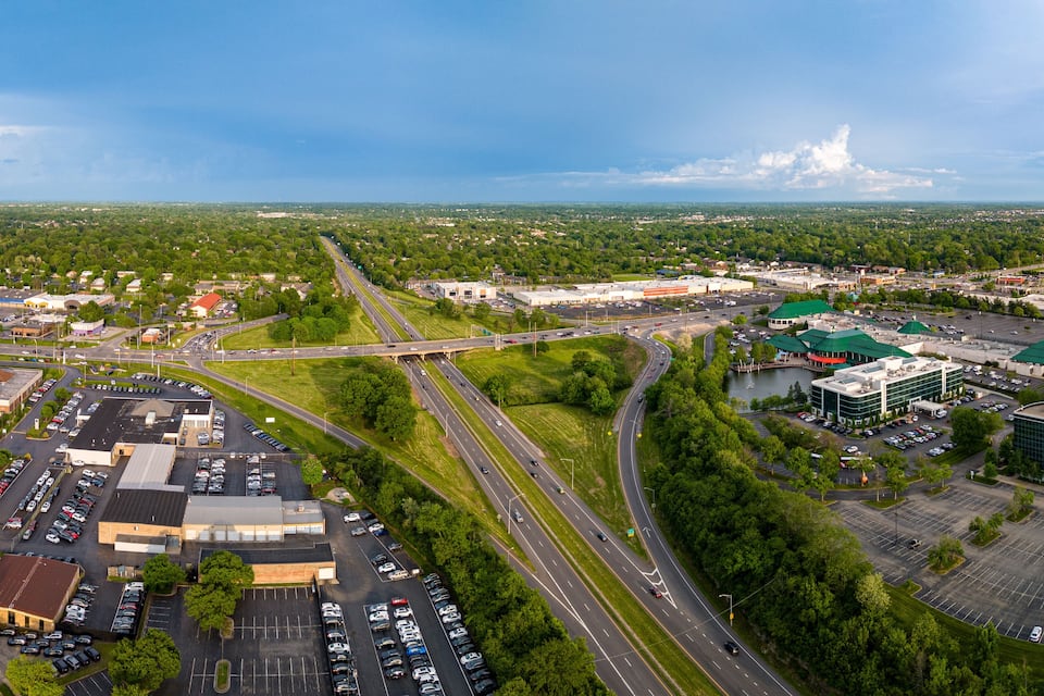 Vista aérea de una ciudad con una autopista, estacionamientos y zonas verdes.