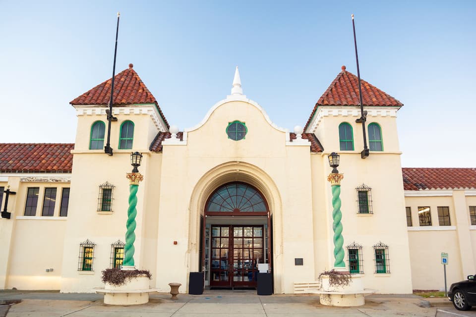 Um edifício histórico com uma entrada central em arco, duas torres e um telhado de telhas vermelhas.