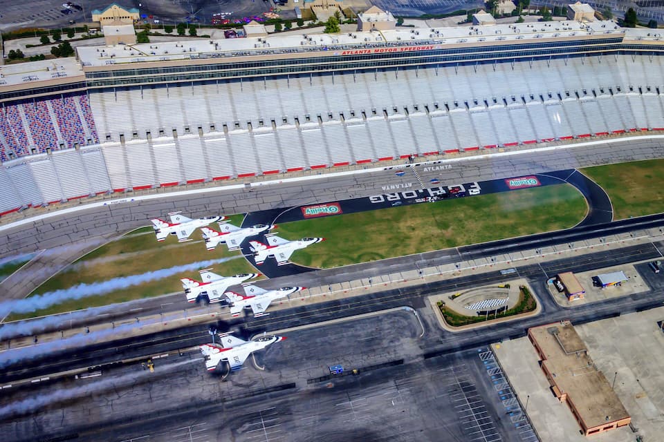 An aerial view of the Atlanta Motor Speedway with multiple race cars on the track and empty grandstands.