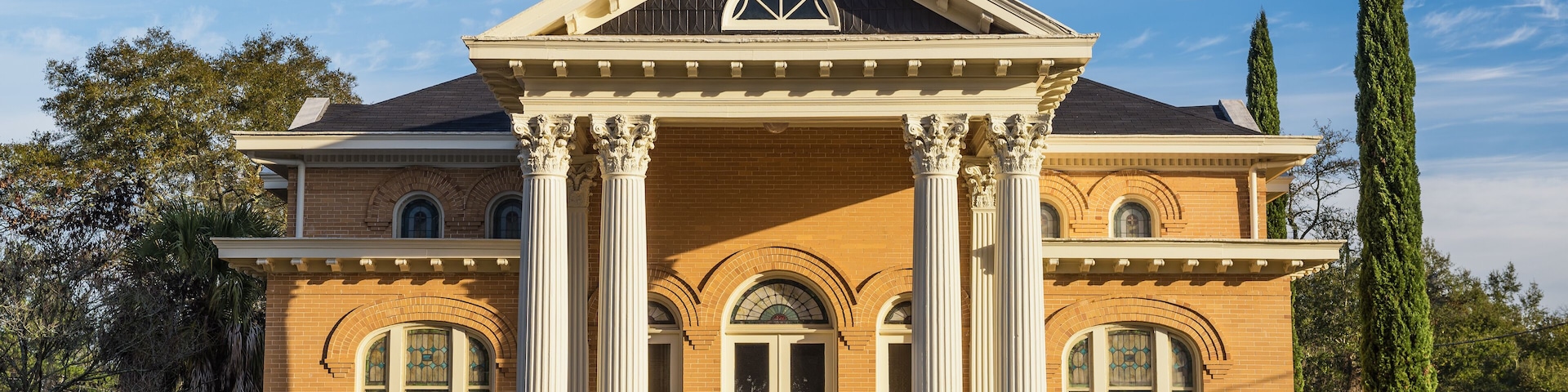 Un edificio grande de dos pisos con una cúpula y columnas, rodeado de jardines y árboles bien cuidados.