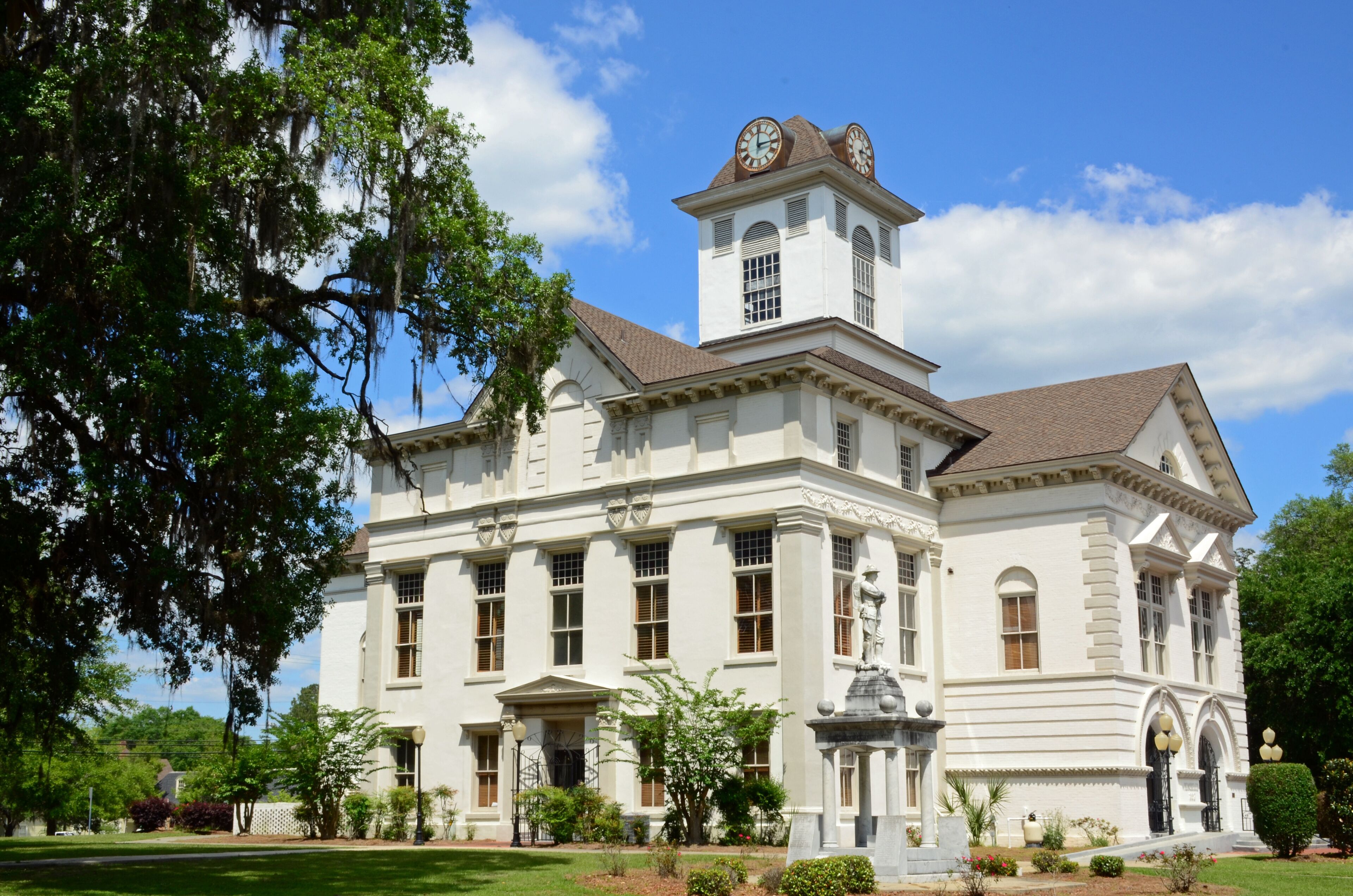 A large white building with a clock tower, surrounded by trees and a well-maintained lawn.