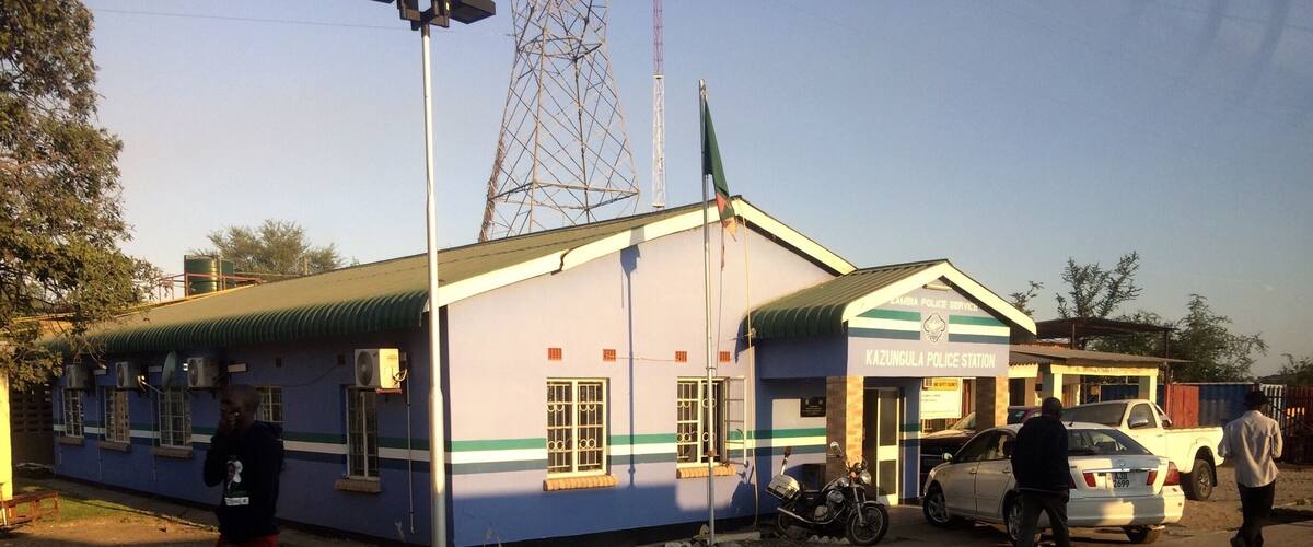 A police station with a blue and white building, a motorcycle, and a white car parked in front.