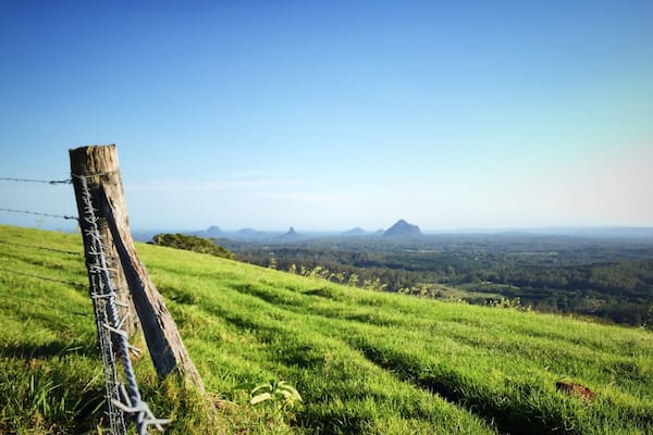 Une colline verdoyante, bordée d’une clôture de barbelés, avec des montagnes lointaines sous un ciel dégagé.