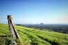 A grassy hillside with a barbed wire fence and distant mountains under a clear sky.