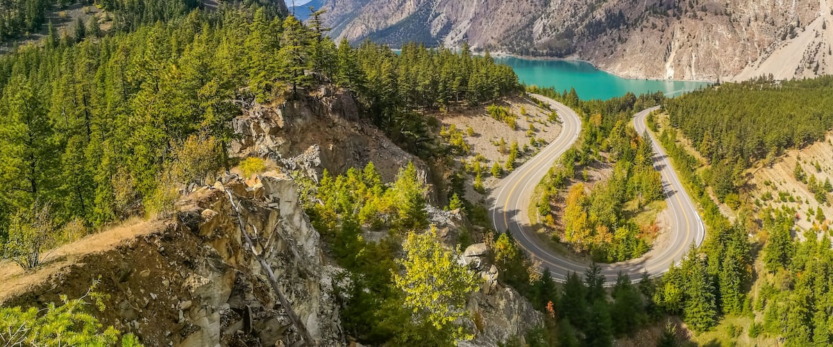 A winding mountain road, a turquoise lake, and forested mountains.
