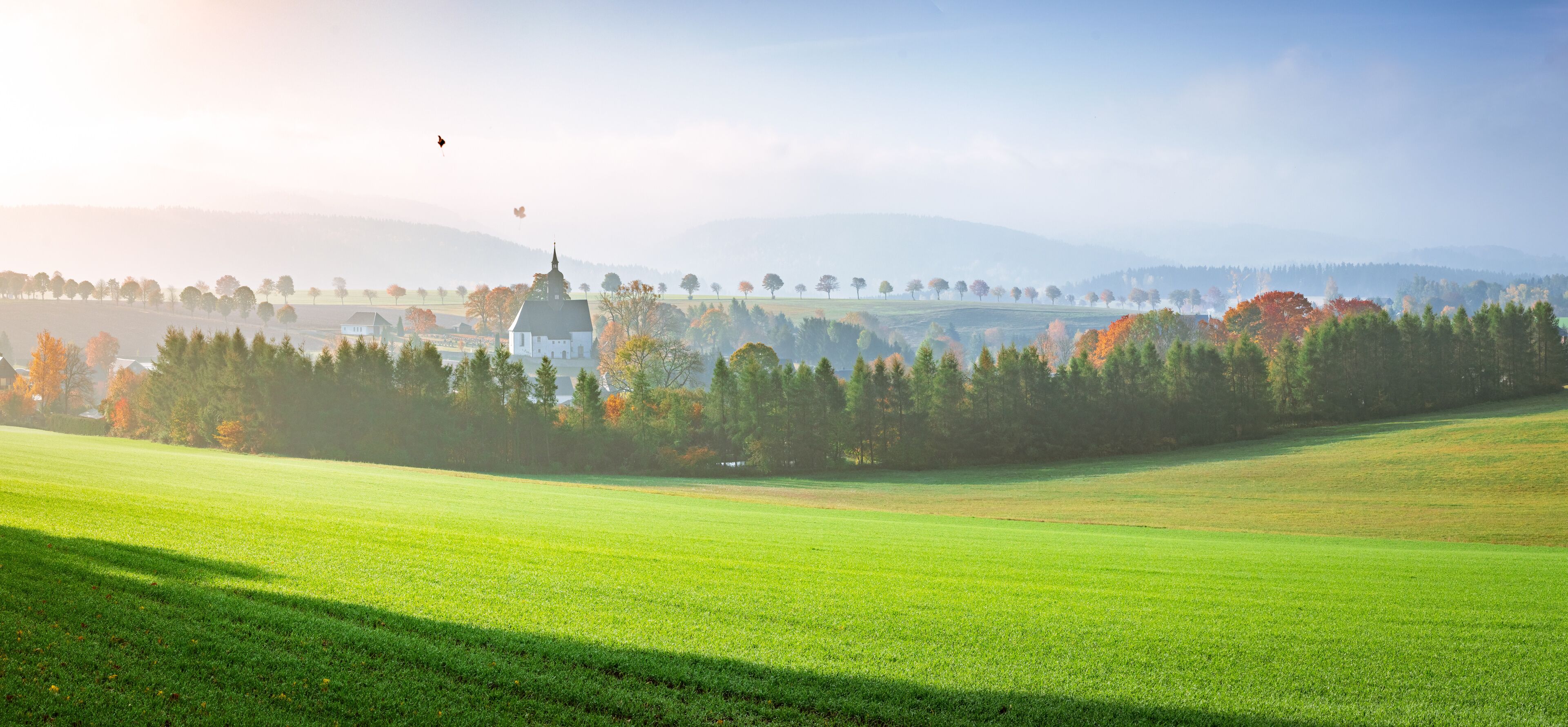 A serene landscape with a church, rolling hills, and a clear sky.