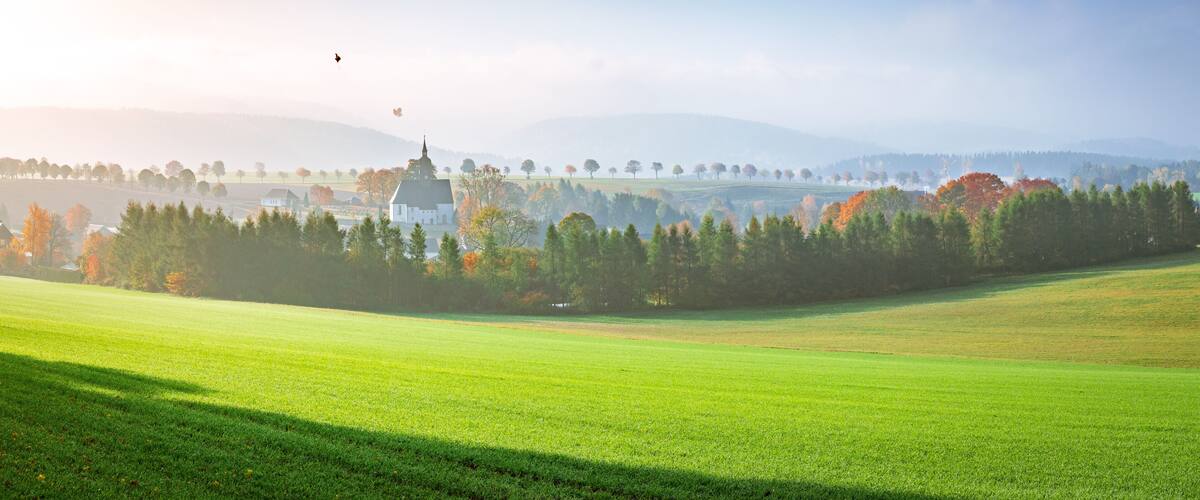 A serene landscape with a church, rolling hills, and a clear sky.