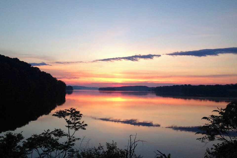 A calm lake at sunset with a forested shoreline and a clear sky.