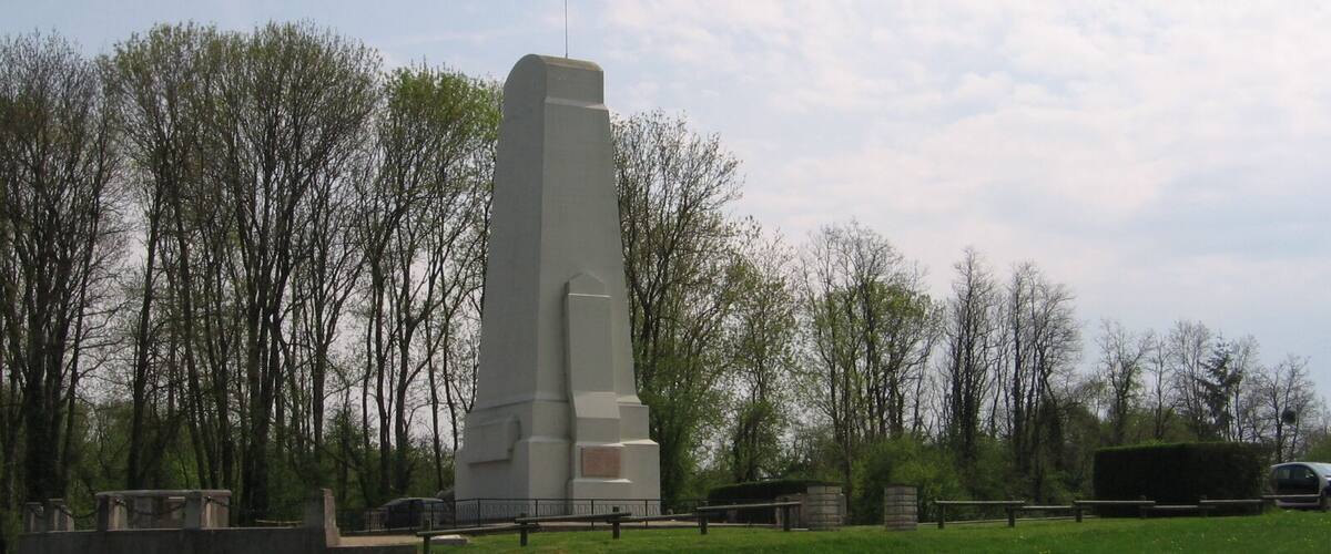 A tall, rectangular monument with a plaque, surrounded by a grassy area and trees.