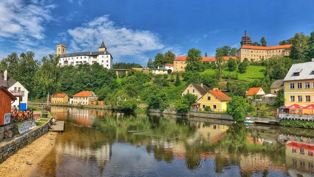 Eine Stadt am Flussufer mit historischen Gebäuden, einer Burg und üppigem Grün.