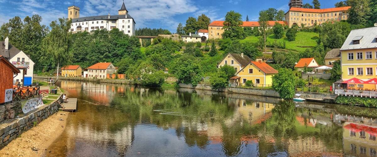 A riverside town with historic buildings, a castle, and lush greenery.