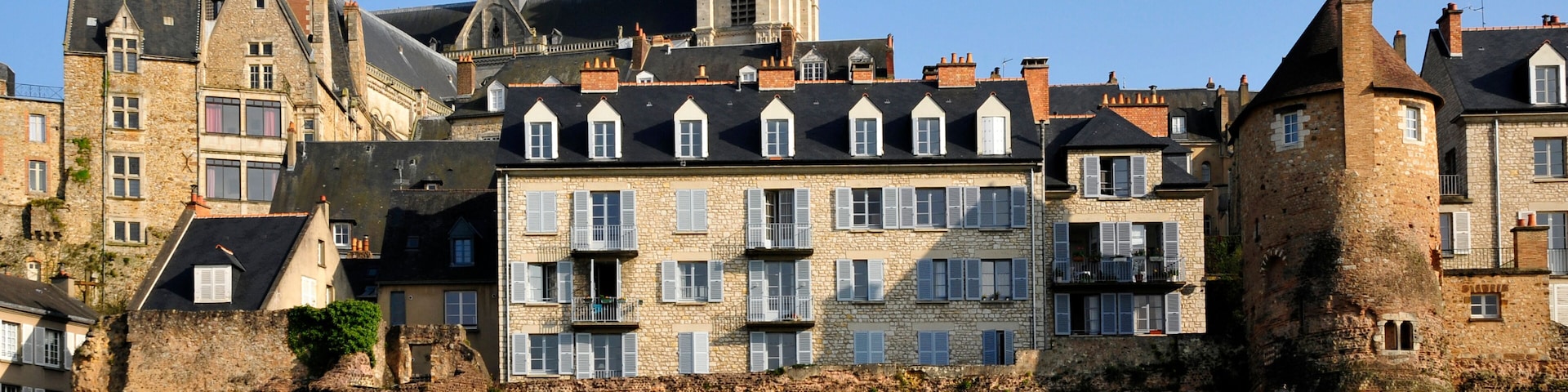 Uma cidade histórica com edifícios de pedra, uma imponente torre do relógio e um caminho de jardim bem cuidado.