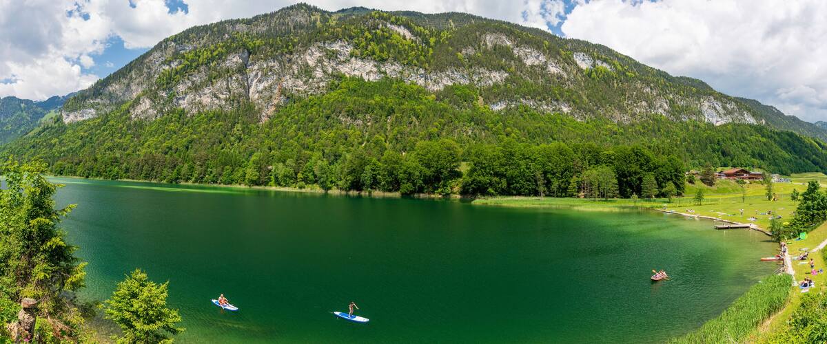 A lake surrounded by mountains, with people kayaking and a dock with boats.