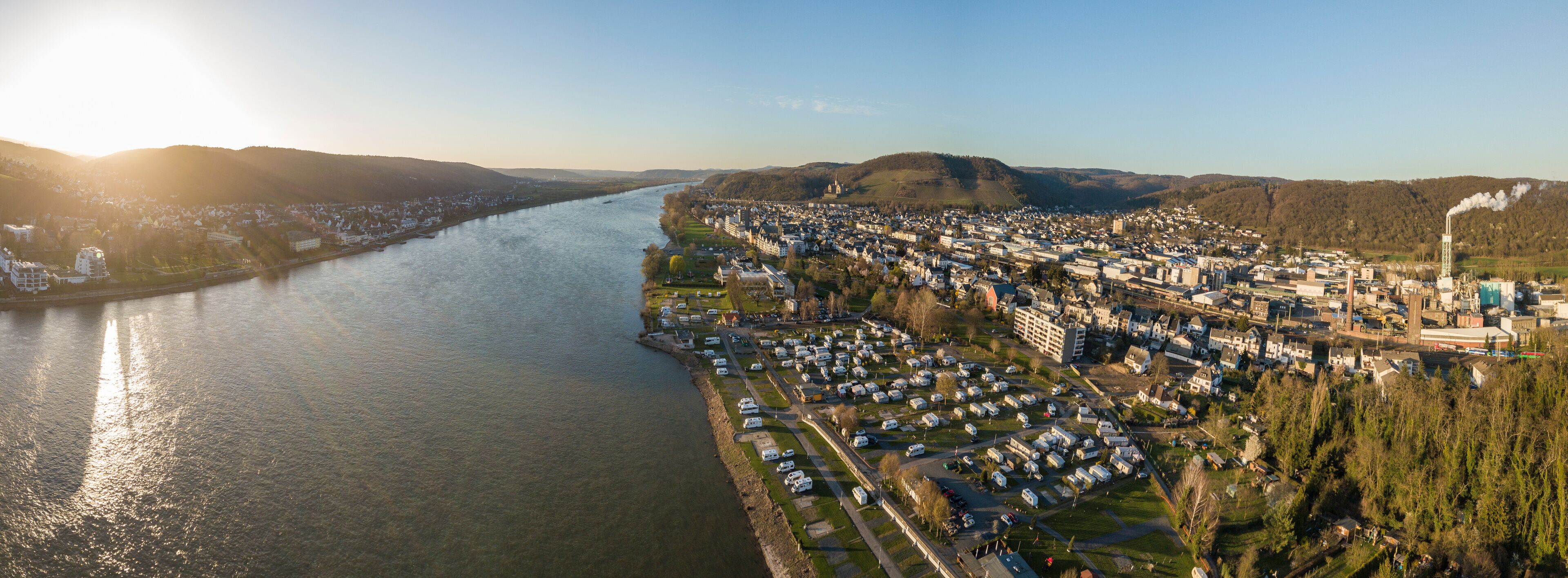 A river flowing through a town with a mix of residential and industrial buildings, surrounded by hills.