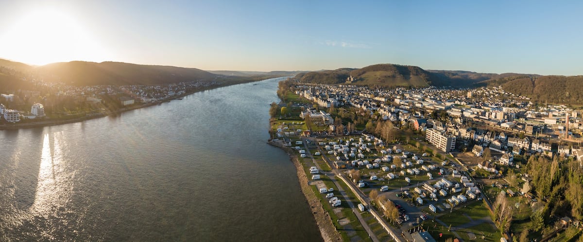 A river flowing through a town with a mix of residential and industrial buildings, surrounded by hills.