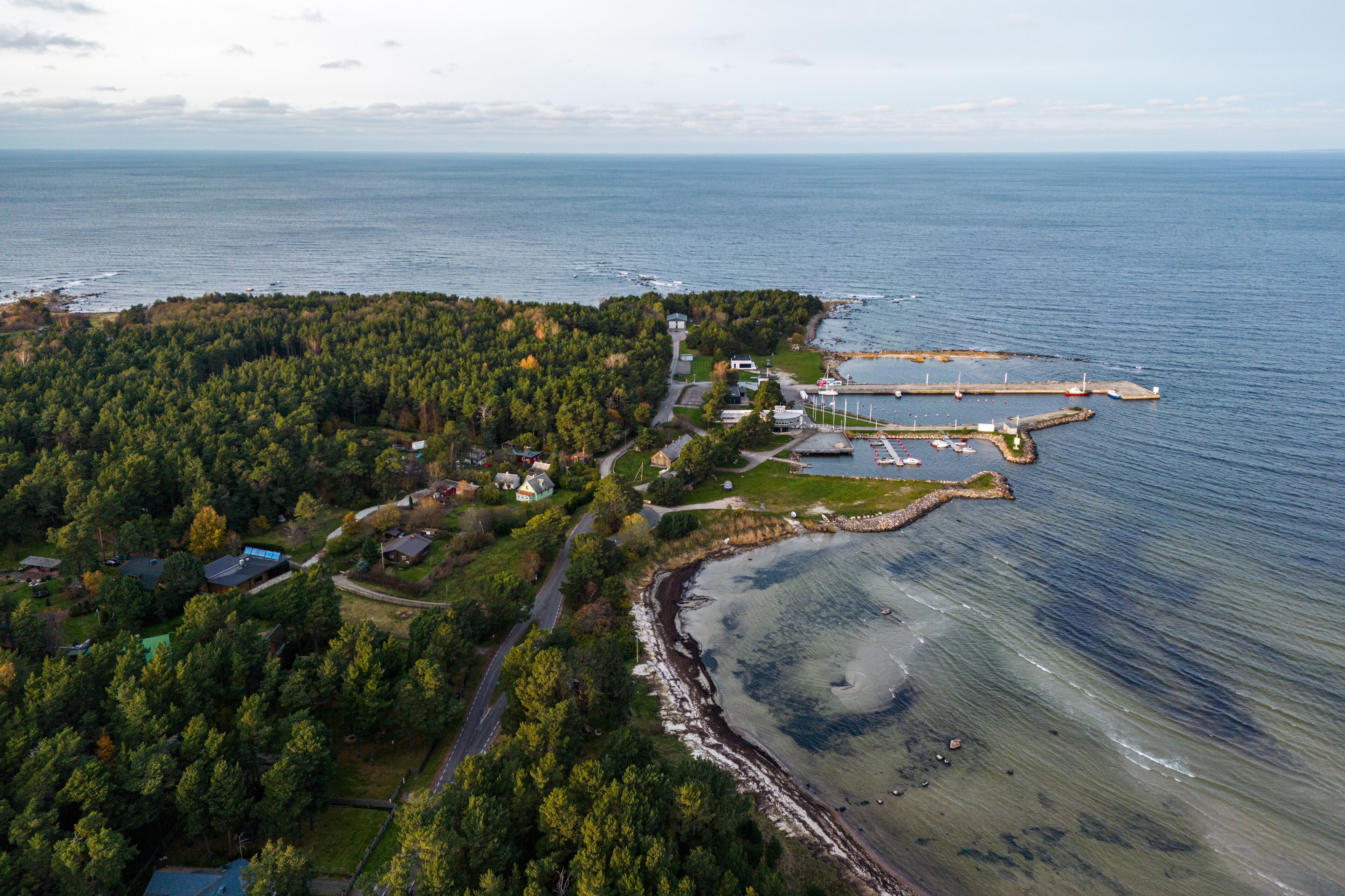 An aerial view of a coastal town with a forested area, a marina, and a lighthouse.