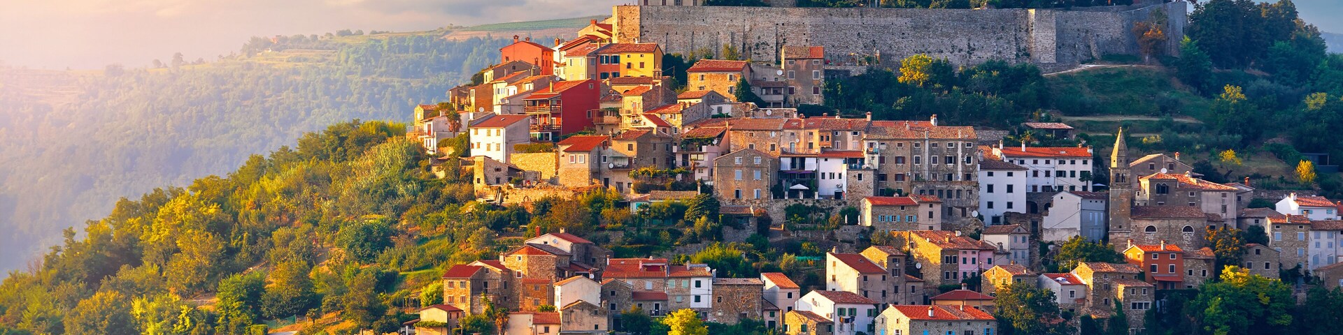 Uma cidade histórica no alto de uma colina, com uma torre imponente e muralhas fortificadas.