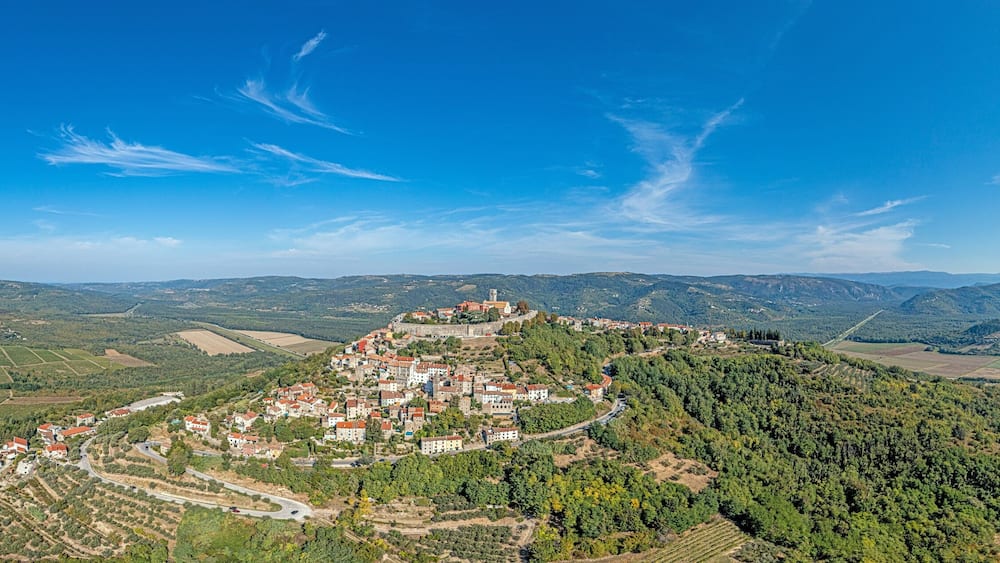 A mountainous landscape with a village nestled in the valley, surrounded by fields and forests.