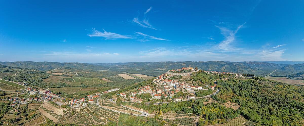 A mountainous landscape with a village nestled in the valley, surrounded by fields and forests.