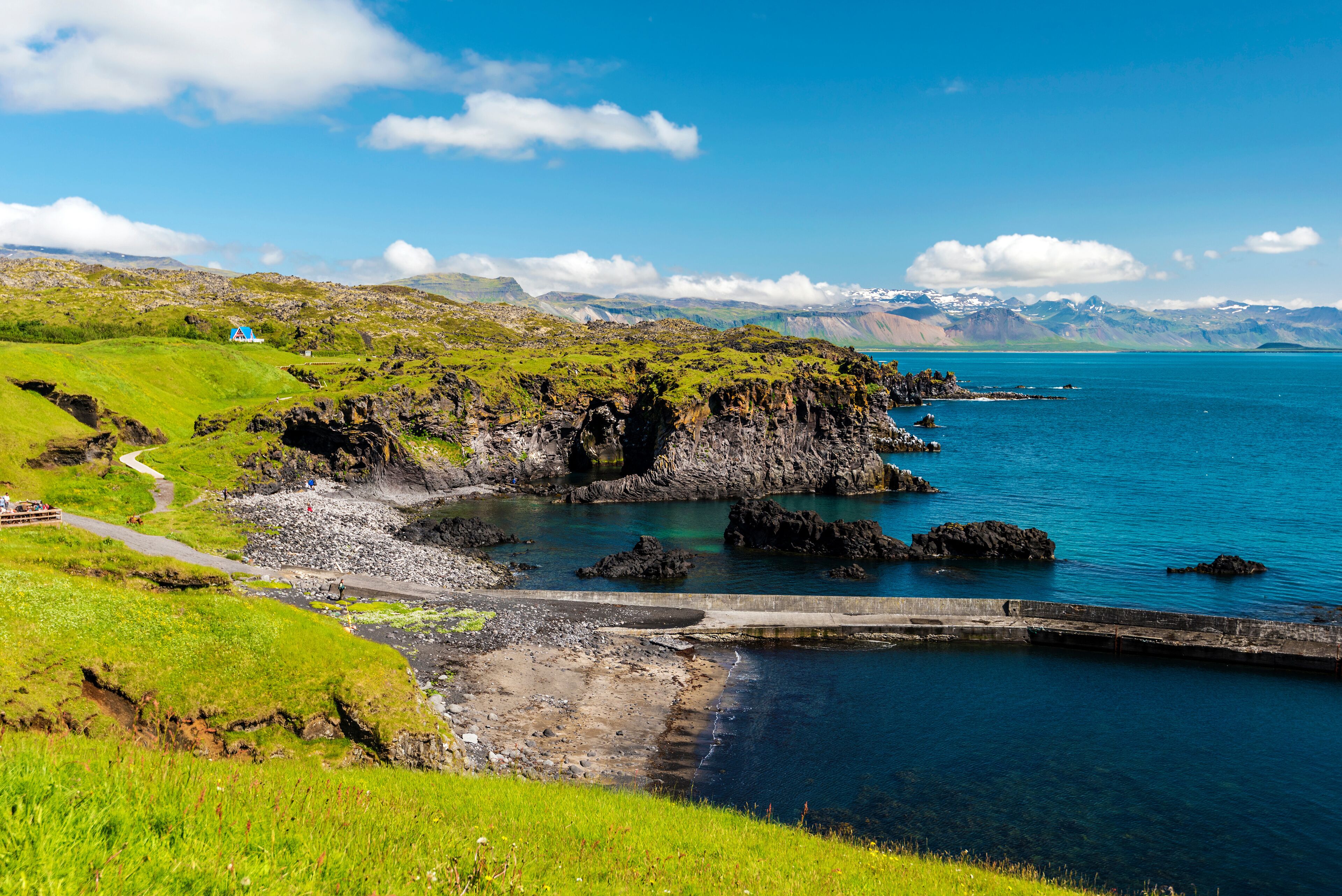 A coastal landscape with green hills, a rocky shoreline, and a clear blue sea.