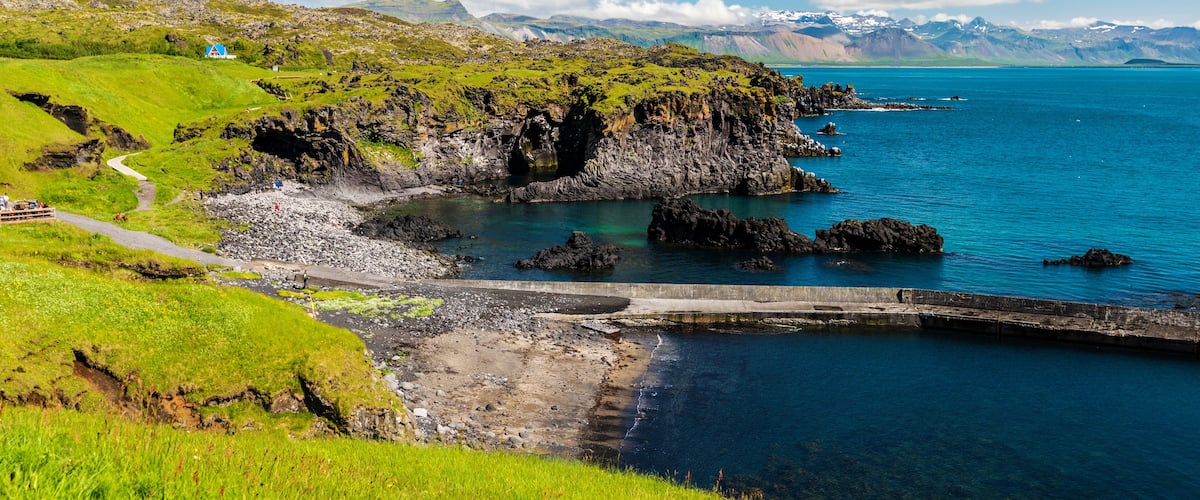 A coastal landscape with green hills, a rocky shoreline, and a clear blue sea.