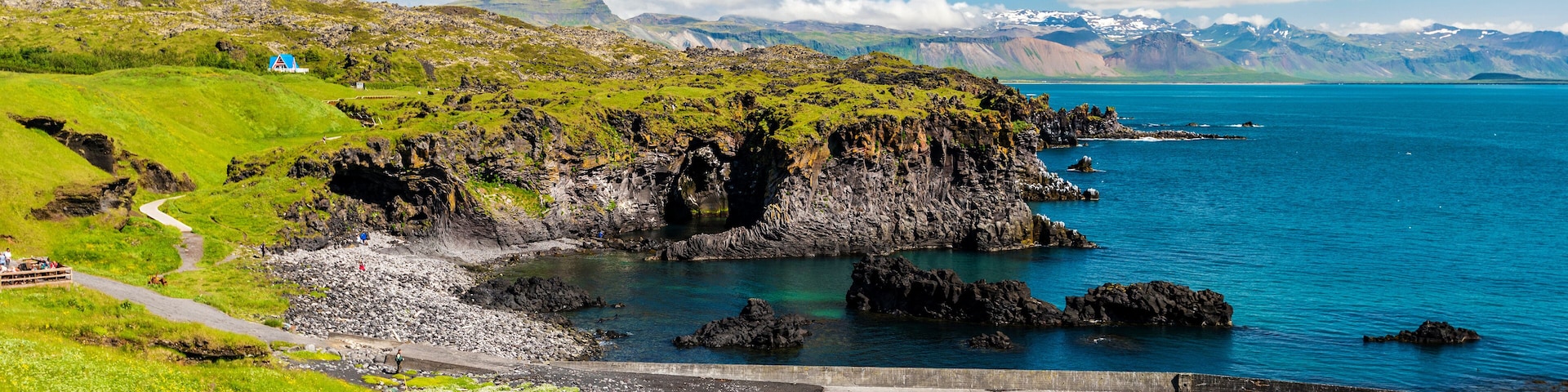 A coastal landscape with green hills, a rocky shoreline, and a clear blue sea.