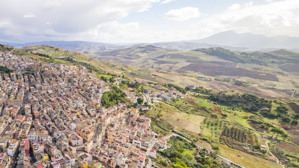 A densely packed town with terraced houses on a hillside, surrounded by rolling hills and fields.