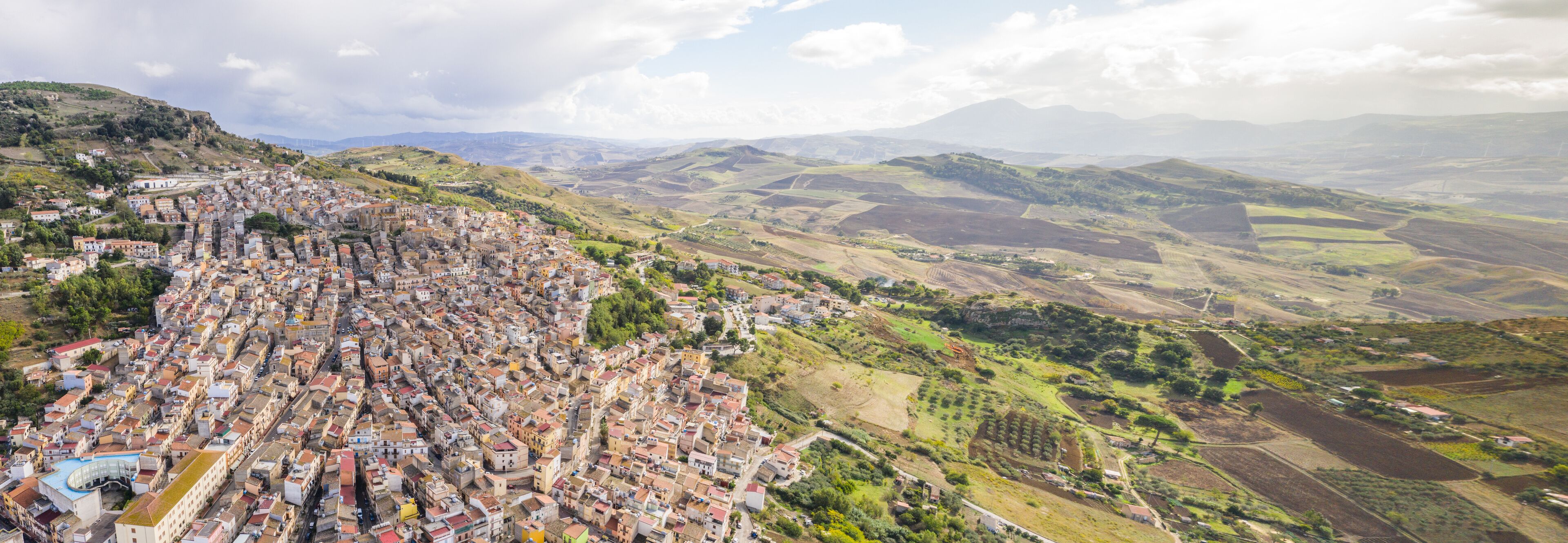 A densely packed town with terraced houses on a hillside, surrounded by rolling hills and fields.