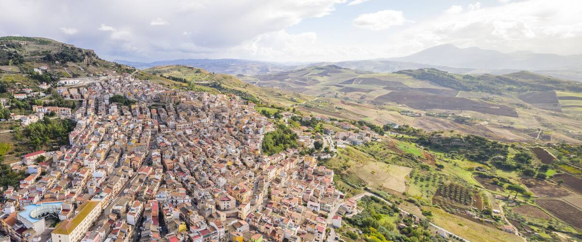 A densely packed town with terraced houses on a hillside, surrounded by rolling hills and fields.