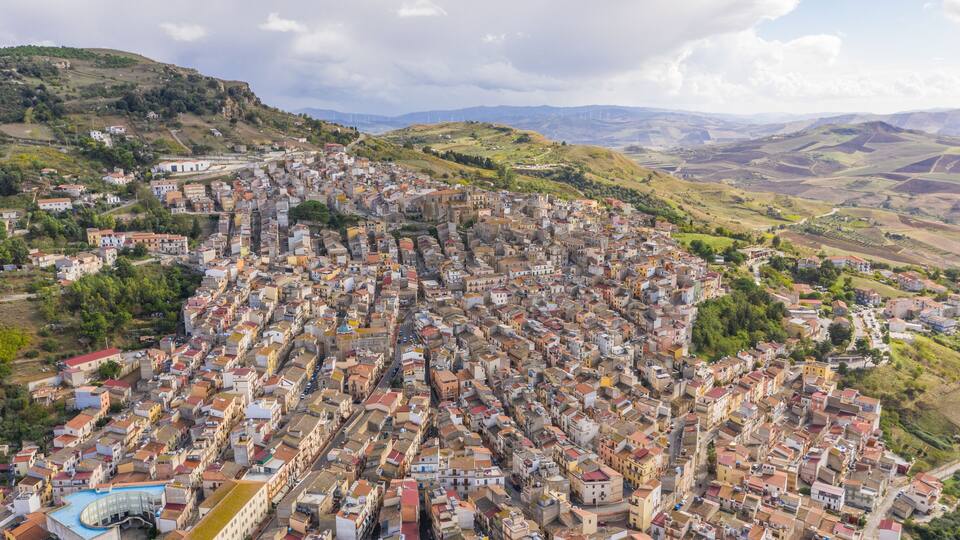 A densely packed town with historic buildings and a hilly landscape in the background.