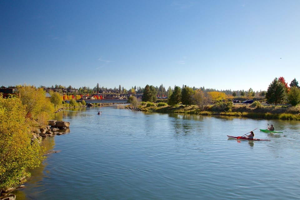 A calm river with kayakers, autumn foliage, and a bridge in the background.