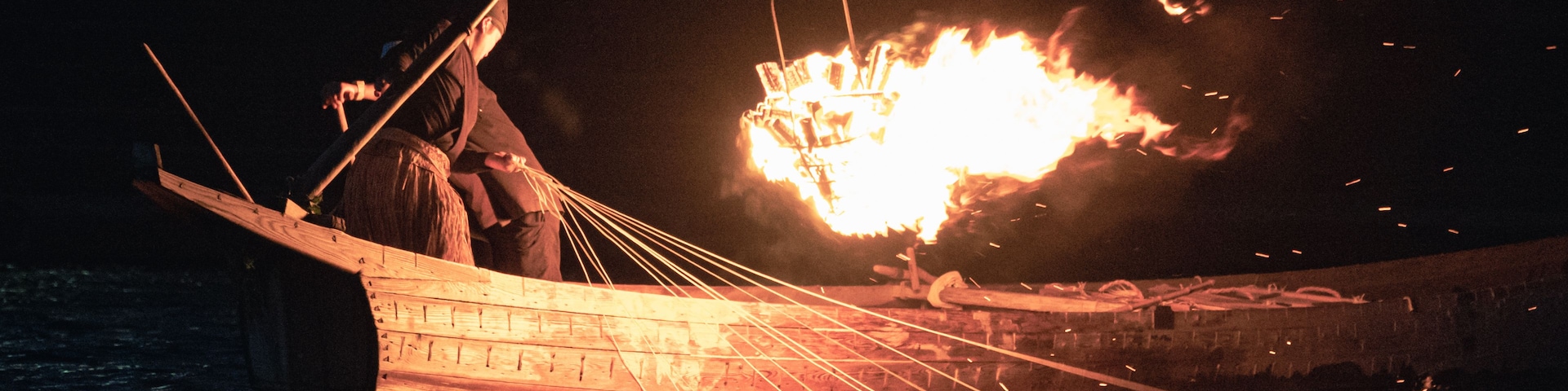 Um barco com um incêndio grande no convés, cercado por água.