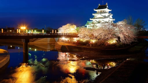 Tourists walking on a bridge toward Sunomata Ichiya Castle which is illuminated at blue dusk and surrounded by beautiful cherry blossom trees (Sakura) during Hanami Matsuri Festival, in Gifu, Japan
