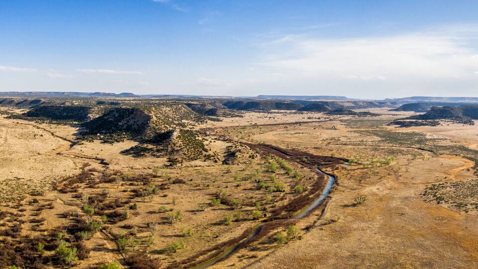 A vast canyon landscape with a winding river and sparse vegetation.
