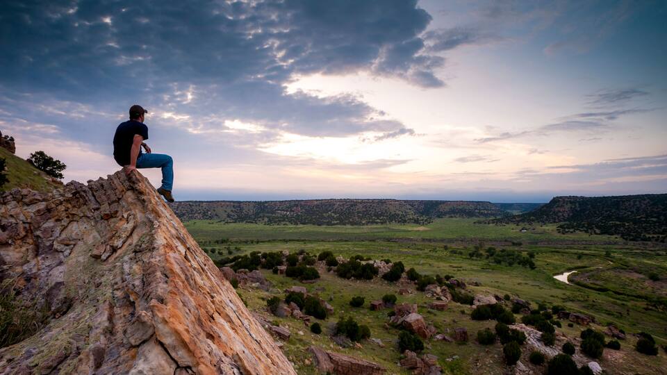 A person sitting on a rocky outcrop overlooking a valley with a winding river.