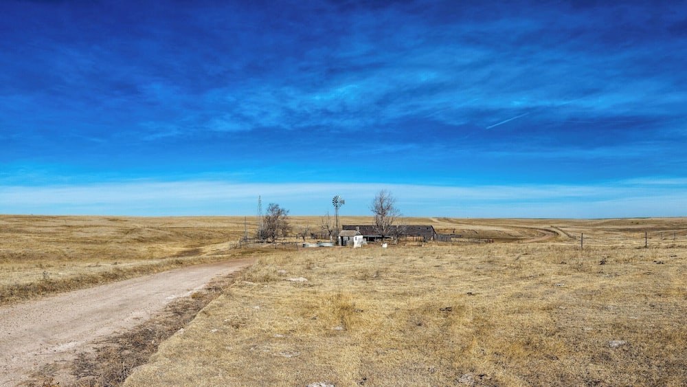A rural landscape with a dirt road, a windmill, and a small building.