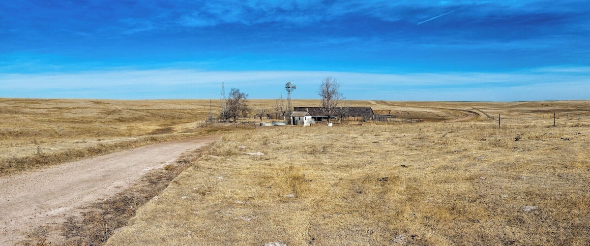 A rural landscape with a dirt road, a windmill, and a small building.