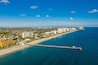 A coastal cityscape with a long beach, a pier extending into the ocean, and high-rise buildings lining the shore.